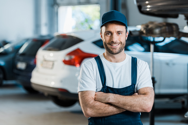 happy car mechanic standing with crossed arms in car service  - Foto, immagini