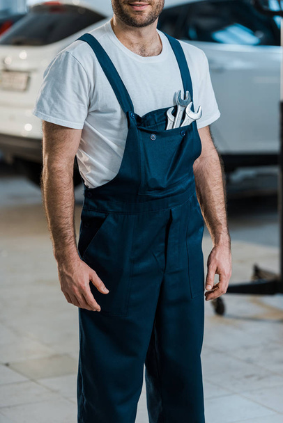 cropped view of happy auto mechanic standing with hand wrenches in pocket  - Foto, Imagem