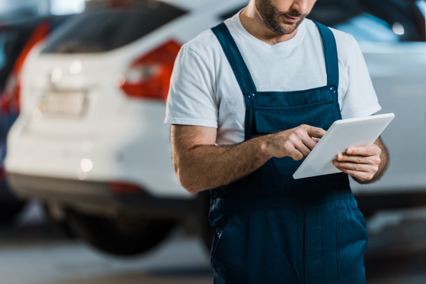 cropped view of car mechanic using digital tablet in car service  - Foto, afbeelding