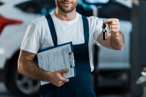 cropped view of car mechanic holding clipboard and key  - Photo, Image