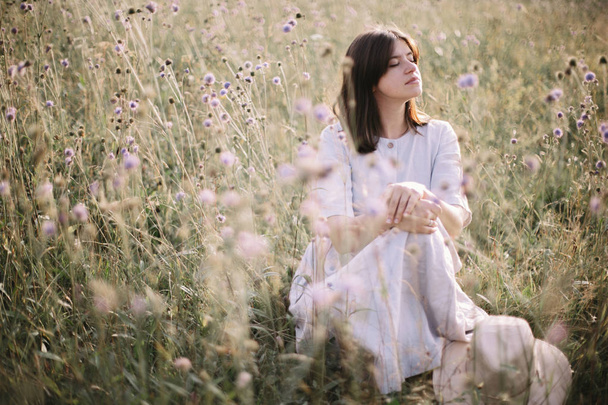 Stylish girl in rustic dress sitting among wildflowers and herbs - Photo, Image