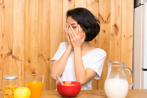 Asiática joven tomando desayuno leche cubriendo los ojos y mirando a través de los dedos
 - Foto, imagen