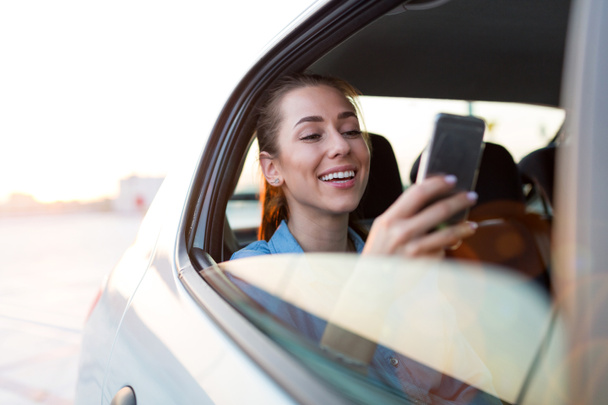 Young woman with smartphone on the back seat of a car - Foto, immagini
