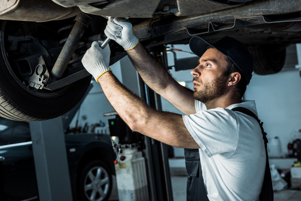 bearded auto mechanic in cap repairing automobile in car service  - Valokuva, kuva
