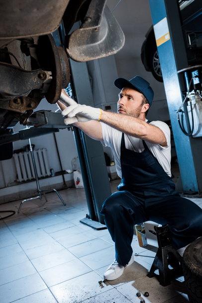 бородатый автомеханик в шапочке и перчатках ремонт автомобиля в автосервисе
  - Фото, изображение