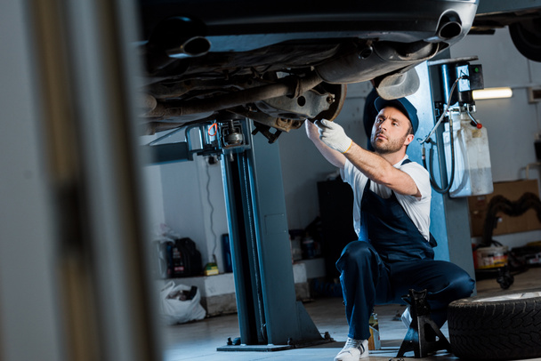 selective focus of auto mechanic in cap and gloves repairing automobile in car service  - Fotó, kép