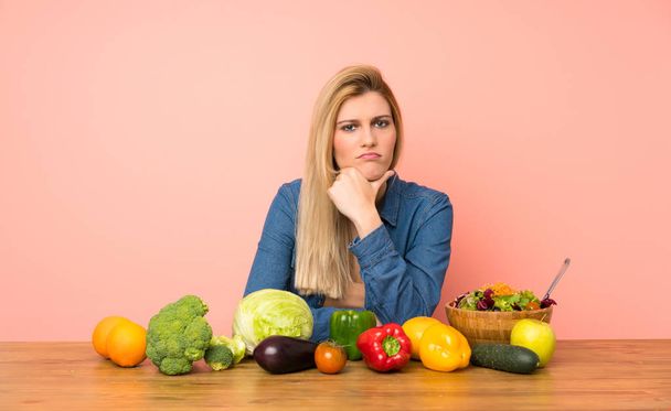 Νεαρή ξανθιά γυναίκα με πολλά λαχανικά σκέφτεται - Φωτογραφία, εικόνα