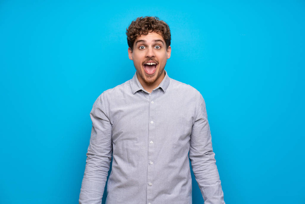 Homme blond sur un mur bleu avec une expression faciale surprise
 - Photo, image