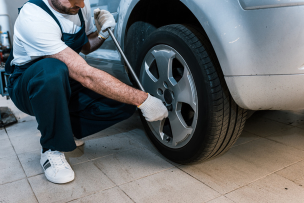  cropped view of auto mechanic in uniform holding metallic wrench near car  - Photo, image
