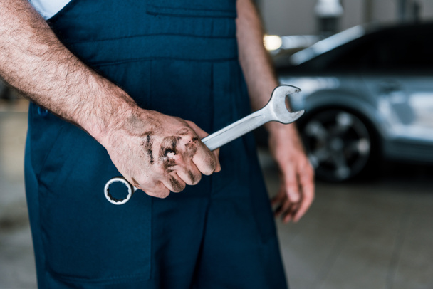 cropped view of auto mechanic with mud on hand holding hand wrench in car repair station  - Fotoğraf, Görsel