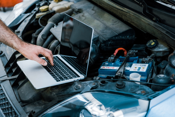 abgeschnittene Ansicht von Automechaniker mit Laptop mit leerem Bildschirm in der Nähe des Autos  - Foto, Bild