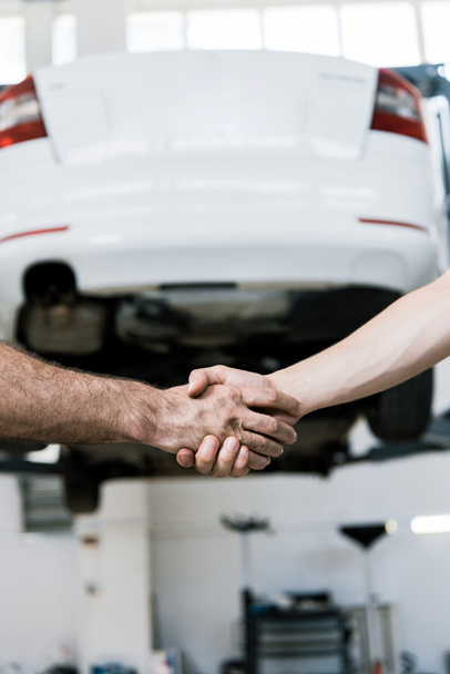 Ausgeschnittene Ansicht von Automechaniker beim Händeschütteln mit Mann in Garage  - Foto, Bild