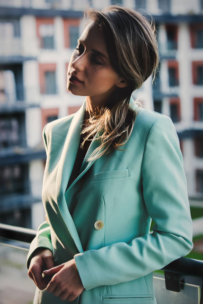 Mooie vrouw in blauwe jas op balkon van appartementen - Foto, afbeelding