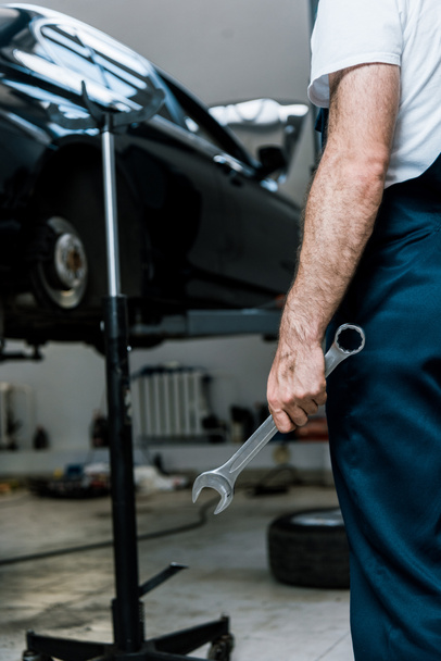 bijgesneden beeld van reparateur vasthouden hand moersleutel in auto reparatie station  - Foto, afbeelding
