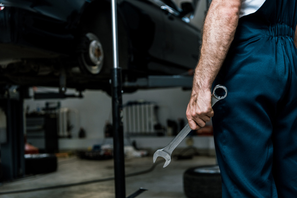 Ausgeschnittene Ansicht eines Automechanikers, der einen Handschlüssel in einer Autowerkstatt hält  - Foto, Bild