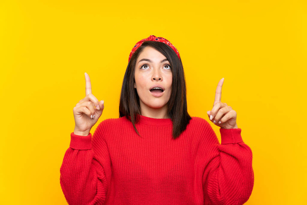Giovane donna messicana con maglione rosso sul muro giallo che punta con l'indice una grande idea
 - Foto, immagini