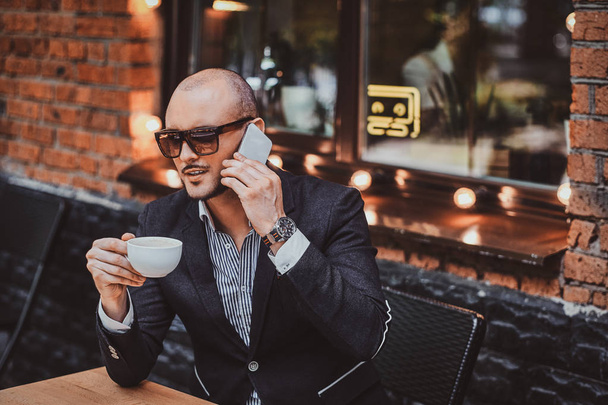Serious sucessful man is calling by mobile and enjoying his coffee. - Zdjęcie, obraz