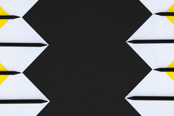 Adesivos brancos e amarelos com lápis pretos forrados com um padrão geométrico em um fundo preto
 - Foto, Imagem