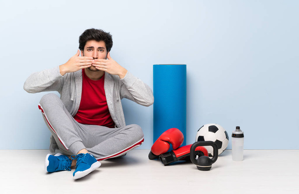 Sport man sitting on the floor covering mouth with hands - Φωτογραφία, εικόνα