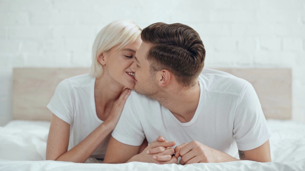 hermosa sonriente pareja cogida de la mano, hombre mordiendo la mano y besar a la mujer en la cama
 - Metraje, vídeo