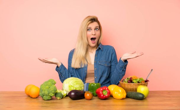 Young blonde woman with many vegetables with shocked facial expression - Foto, Bild