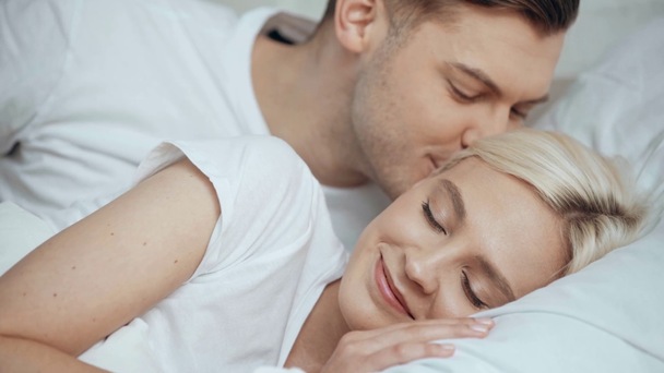 handsome man embracing and waking up beautiful sleeping woman with kissing in bed - Filmati, video