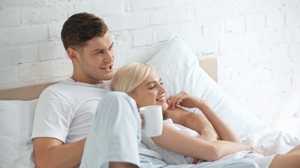 hermosa pareja sonriendo, abrazando y hablando en la cama, hombre bebiendo café
 - Metraje, vídeo
