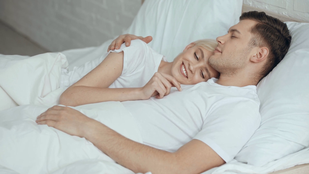 красивая женщина гладит и обнимает улыбающегося спящего мужчину в постели
 - Кадры, видео