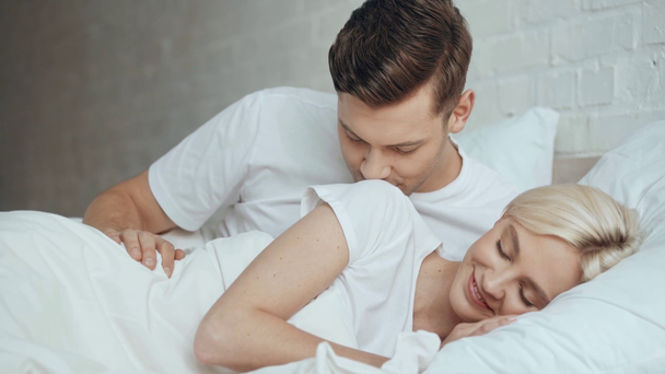 schöner Mann umarmt und weckt schlafende Frau mit Küssen im Bett - Filmmaterial, Video