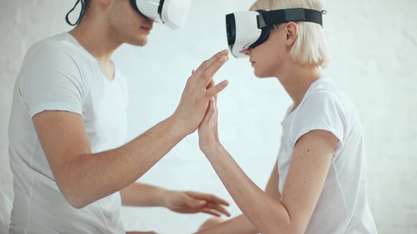 Paar in Virtual-Reality-Headsets hält sich an Händen und gestikuliert zu Hause - Filmmaterial, Video