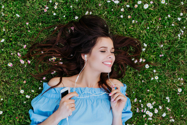 Beautiful woman listening to music with headphones and lying in a garden of flowers - Photo, Image