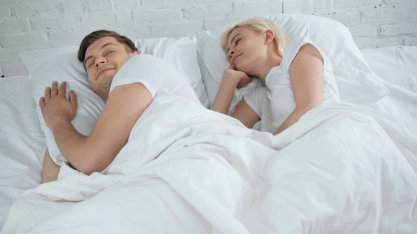 beautiful young woman kissing sleeping man, boyfriend waking up and kissing girlfriend in bed - Felvétel, videó