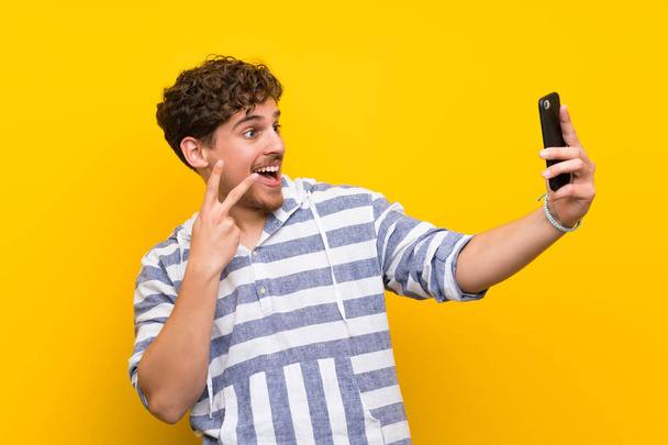 Blonde man over yellow wall making a selfie - Foto, afbeelding