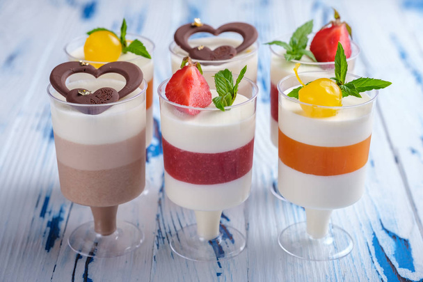 Six mousse desserts in wineglasses, decorated chocolate, strawberry, mint and cocktail cherries on aged wooden table. - Photo, Image