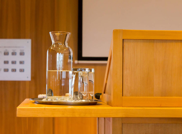 Wooden trubune in a conference or lecture hall with a water pitcher and a white projector screen - Photo, Image