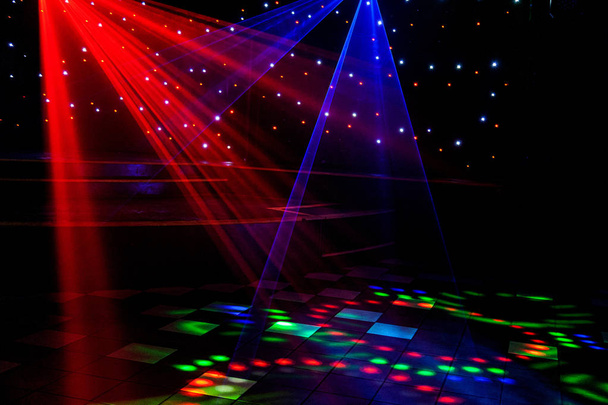 Las luces láser de discoteca brillantes cortan el humo de la máquina de humo haciendo patrones de luz y arco iris en la pista de baile. Luces láser con bokeh en el fondo. Inspiración para promociones de Mardi Gras o nightlcub
. - Foto, Imagen