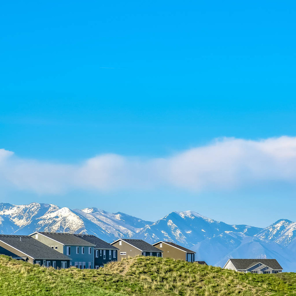 Square frame Residences on a hill against snow capped mountain and blue sky with clouds - Photo, Image