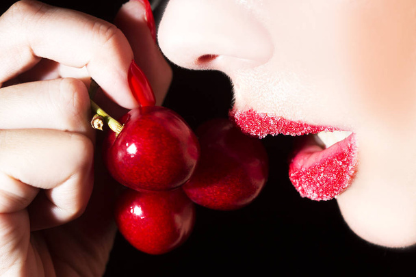 Sexy woman eating cherry. Sensual red lips in sugar isolated on black background. - Foto, Imagem