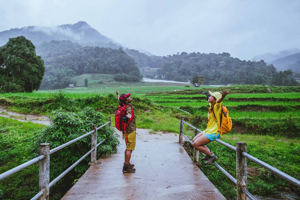 Szerető ázsiai ember ázsiai nők utazási természet. Walking egy fotót a rizs területén, és megáll egy kis szünetet pihenni a hídon a tilalom Mae Klang Luang az esős évszak. - Fotó, kép