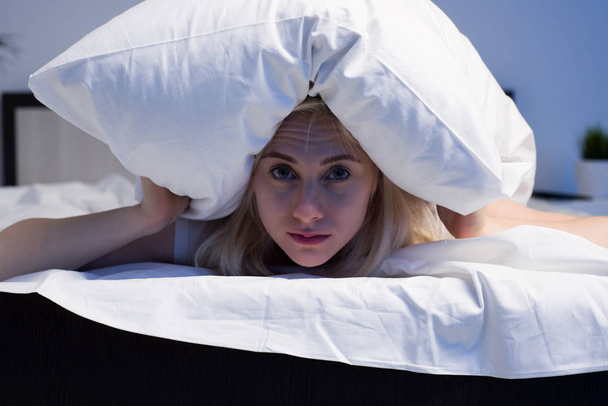 Mujer acostada en la cama y cerrando las orejas con almohada - Foto, Imagen