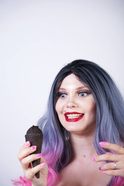 goth girl eating black ice cream in waffle cone. hot plus size woman wearing satin corset with pink bows and enjoys fresh cold tasty sweet ice-cream on white studio background.  - Фото, зображення