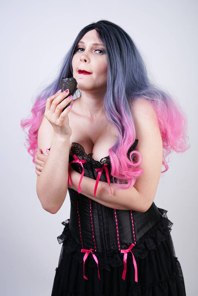 goth girl eating black ice cream in waffle cone. hot plus size woman wearing satin corset with pink bows and enjoys fresh cold tasty sweet ice-cream on white studio background.  - Fotografie, Obrázek