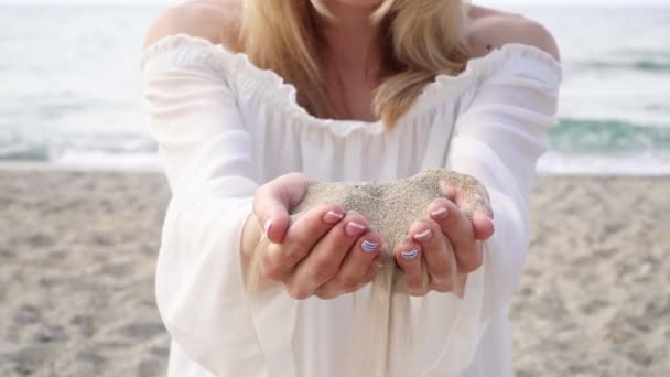 Een vrouw houdt zand in haar palmen, zand giet door haar vingers. - Video