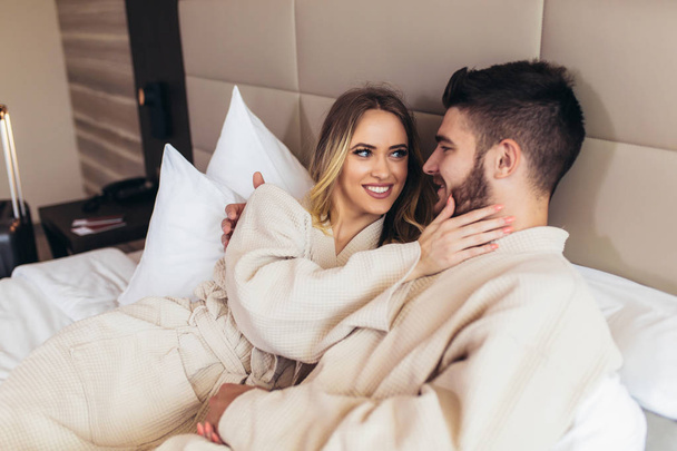 Jovem casal amoroso em roupões de banho relaxante na cama do hotel
 - Foto, Imagem