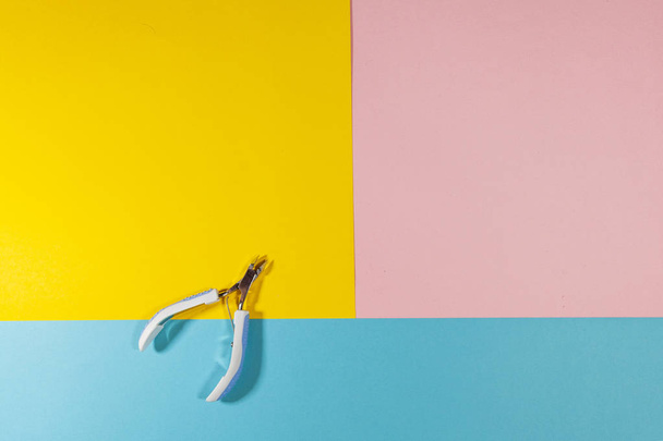 Кусачки для нігтів лежать на плоскій поверхні кольорів рожевого, жовтого і синього
 - Фото, зображення