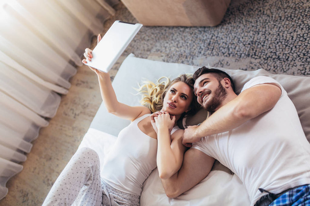 glückliches junges Paar liegt auf dem Bett im Schlafzimmer und benutzt Ziffer - Foto, Bild