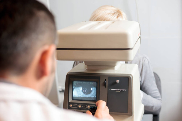 Male ophthalmologist performing eye exam using eye scanner, looking at patients retina on a screen - Foto, afbeelding
