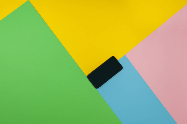 Musta puhelin makaa tasaisella pinnalla vihreä, sininen, vaaleanpunainen, ja keltainen
 - Valokuva, kuva
