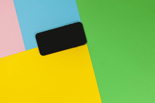 Un teléfono negro está tendido en una superficie plana de verde, azul, rosa y amarillo
 - Foto, Imagen