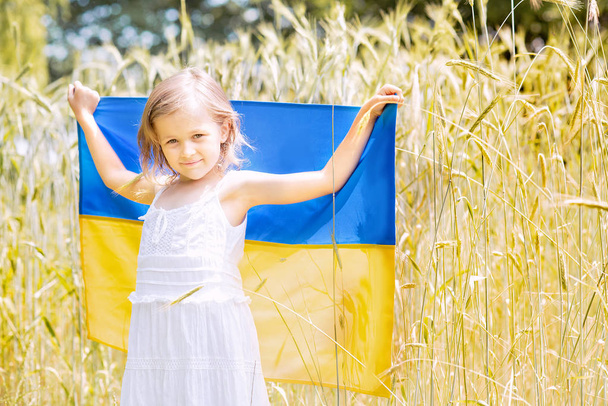 little girl carrying fluttering blue and yellow flag of Ukraine in wheat field, Ukraine Independence Day concept - Fotó, kép